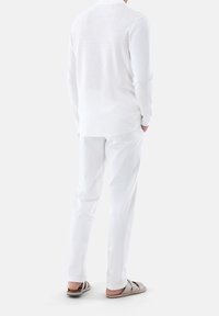 Biały, długi sweter z dzianiny o otwartym splocie, zestawiony z białymi, dopasowanymi spodniami i brązowymi sandałami. Skupienie na czystych liniach i przewiewnej fakturze.