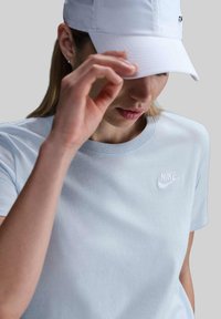 T-shirt di cotone azzurro chiaro con scollo rotondo e logo Nike bianco ricamato sul petto; abbinato a un cappellino bianco.