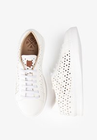 Zapatillas blancas con patrones geométricos recortados, cordones blancos y un acento de cuero beige. Suela plana y diseño casual. Material duradero.