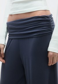 Tumši zili, viegli svārki ar saspiestu vidukli. Kombinēti ar piegulošu baltu garroku topu ar ribotu faktūru.