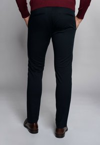 Czarne spodnie slim-fit wykonane z miękkiego materiału, z płaskim przodem, tylnymi kieszeniami i noszone z brązowymi skórzanymi butami.