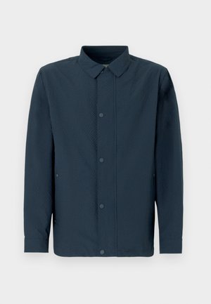 Tumesinine pika varrukaga särk tekstuurse kangaga, esikinnitatud nööpide, klassikalise krae ja küljetaskutega, taustal ühevärviline.