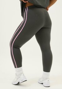 Grå leggings med rosa sidostreck. Tillverkade av elastiskt material, vilket ger en åtsittande design. Bärs med vita sneakers och strumpor.