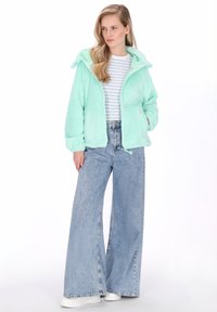 Menta zöld, puha kabát kapucnival, elöl cipzárral és zsebekkel, csíkos inggel és magas derekú, bőszárú farmernadrággal párosítva.