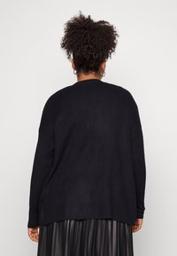 Suéter negro de punto con un corte holgado, dobladillo acanalado y mangas largas, combinado con una falda negra plisada. Textura suave y diseño minimalista.