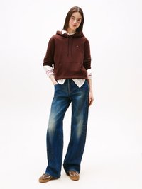 Sweatshirt com capuz numa tonalidade castanho-avermelhada, com bolso frontal, combinado com jeans de perna larga em azul claro, apresentando um design desbotado, e sapatos de slip-on castanhos.