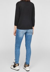 Black long-sleeve top, blue skinny jeans, and chunky sneakers with a mix of beige, black, and white accents. Smooth fabric texture.