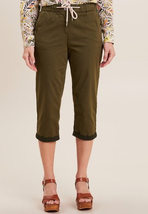 Olijfgroene cropped broek met een trekkoord in de taille, opgerolde broekspijpen en een gladde textuur. Gepaard met bruin plateau-sandalen.