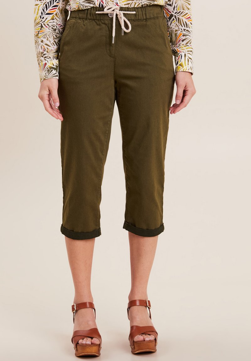 Pantaloni verde oliva a vita alta, con coulisse, orli arrotolati e una texture liscia. Abbinati a sandali con platform marroni.