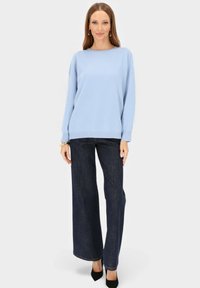 Jasnoniebieski, luźny sweter z okrągłym dekoltem, zestawiony z ciemnoniebieskimi szerokimi dżinsami i czarnymi szpilkami, na białym tle.