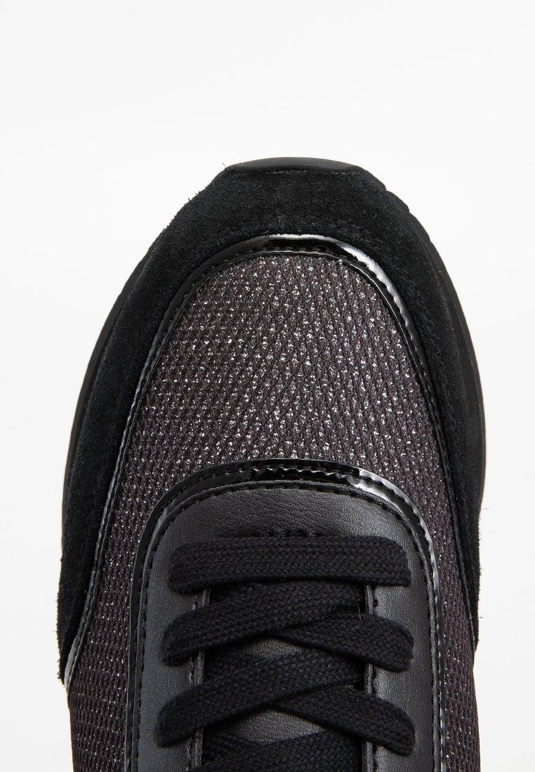 Schwarzer Sportschuh mit einem strukturierten Mesh-Obermaterial, Wildlederakzenten und glänzenden schwarzen Lederdetails. Schnürdesign mit verstärkter Zehenkappe.