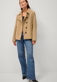 Beige uldblanding frakke med slidsekrave, fem sorte knapper og sidelommer, parret med blå flagrende jeans og sorte hæle.