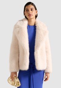 Faux fur jakke i lys lyserød med en bred krave og lange ærmer, parret med en blå kjole og en metallic guld clutch taske.