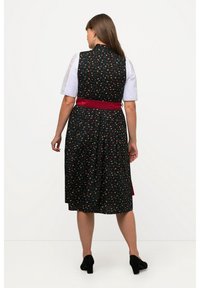 Robe noire avec un motif floral coloré, sans manches, et une ceinture rouge. Des manches blanches avec des détails en dentelle rehaussent l'apparence générale.
