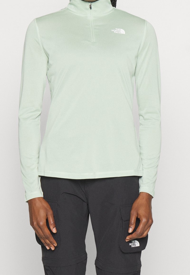 Jasnozielona, długosleeve'owa koszula z zamkiem na szyi, wykonana z gładkiego materiału. Ma małe białe logo na lewej stronie klatki piersiowej.