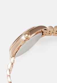 Montre-bracelet en or rose avec un boîtier rond lisse, une couronne texturée et un bracelet à maillons avec des accents arrondis. Le dos est en argent.
