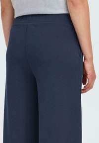 Wide-leg dark navy pants with a smooth texture, featuring a flat waistband and side pockets, viewed from the back.