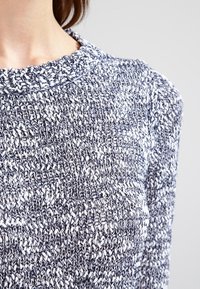 Kevyt, teksturoitu neulepusero, jossa on tummansinivalkoinen kuvio, pyöreä pääntie ja hienovaraiset resorireunukset.