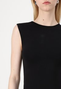Svart ermeløs topp med glatt tekstur, tettsittende design og rund halslinning, med minimal søm og ingen synlige dekorasjoner.