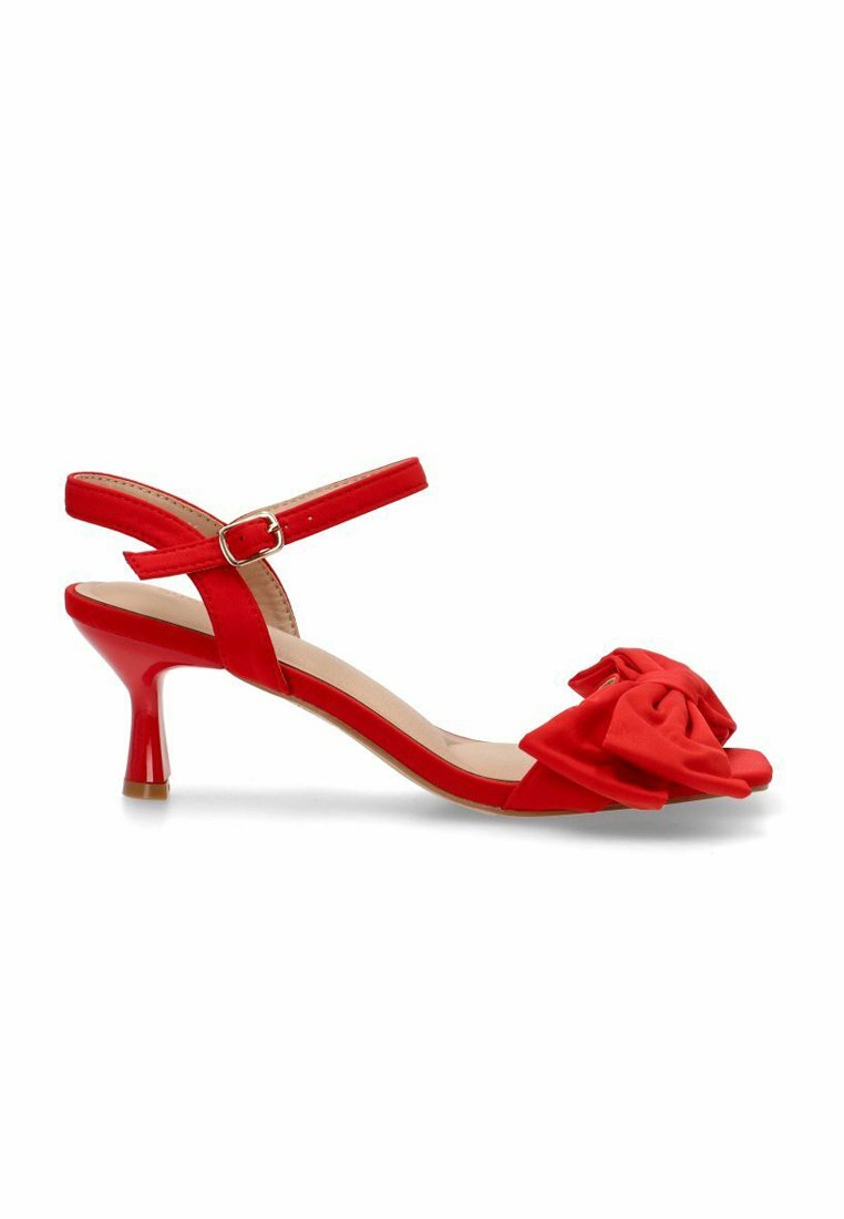 Tacón slingback rojo con la punta descubierta, un lazo de tela en la parte delantera, una correa delgada en el tobillo y un tacón brillante que mide aproximadamente 5 cm.
