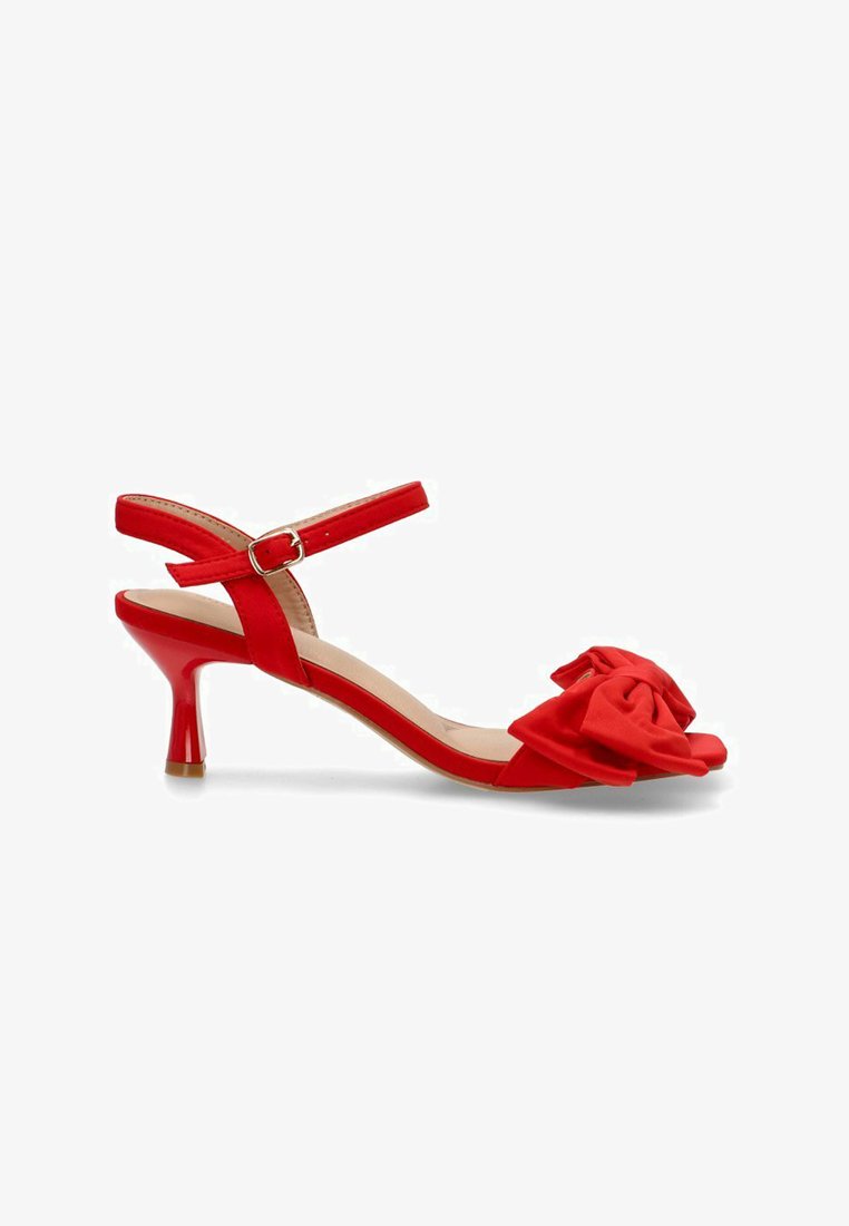 Tacón slingback rojo con la punta descubierta, un lazo de tela en la parte delantera, una correa delgada en el tobillo y un tacón brillante que mide aproximadamente 5 cm.