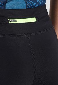Leggings athletic neri con una superficie liscia, dotati di una tasca con zip e un luminoso accento verde neon in vita.
