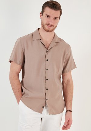 Camisa de manga corta en color beige claro, hecha de una tela suave. Cuenta con un cuello clásico, botones frontales y un corte relajado.