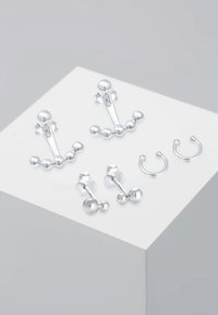 Juego de pendientes de plata que incluye pendientes de botón con acentos esféricos, aros huggie curvados y diseños de gota únicos sobre una superficie plana.