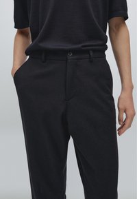 Pantalons en laine noirs avec deux poches latérales, fermeture à bouton, devant plat et design à jambe droite. Tissu texturé avec une finition douce.