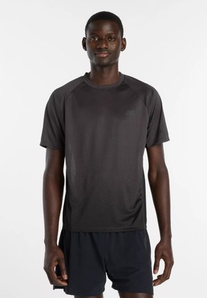 Mies seisoo musta lyhythihaisen urheilupaidan ja mustien shortsien kanssa yksiväristä valkoista taustaa vasten.