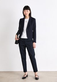 Navy blazer with a single button, paired with a white t-shirt featuring text, dark trousers, and black flats. Simple design with tailored fit.