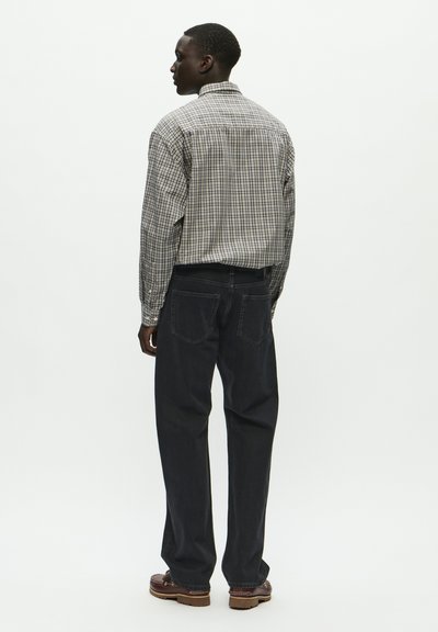 Ruuduline nööpitega särk mustas, valges ja hallis, kombineeritud tumedate teksapükstega. Riietus on lõdva lõikega ja sisaldab delikaatseid õmbluse detaile.