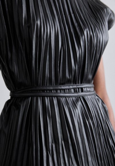 Schwarzes plissiertes Kleid aus glänzendem Stoff, mit engem Oberteil und einem glatten Gürtel, der die Textur und vertikalen Linien betont.