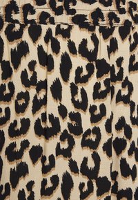 Leopardmönstrad tyg i beige och svart, med en strukturerad yta och djärva, oregelbundna fläckar. Plisserad design med en slät midjeresår.