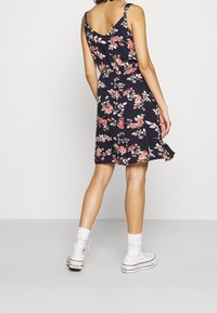 Blumenkleid mit navy Hintergrund, V-Ausschnitt, ärmellos und knielang. Kombiniert mit weißen High-Top-Sneakern und Socken.