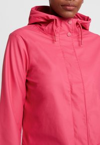 Rosa vattentät jacka med huva, med en slät yta, framknäppningar och justerbara snörningar för en anpassningsbar passform.