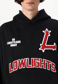 Black hoodie with a front pocket, featuring white and red embroidered text: "99 LIGHTYEARS AWAY" and "LOWLIGHTS," with a red star accent.