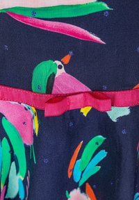 Kwiatowa sukienka z ciemnoniebieskiego materiału, z kolorowymi wzorami ptaków i różową kokardą w talii. Tekstura wydaje się gładka.