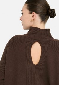 Brązowy sweter z dzianiny z wysokim kołnierzem i wyraźnym owalnym wycięciem na plecach, prezentujący teksturowane prążkowanie wzdłuż szwów.