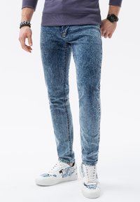 Ljusblå denimjeans med en urblekt textur, smal passform och femficksdesign. Kombineras med vita sneakers med blå och svarta grafiska detaljer.