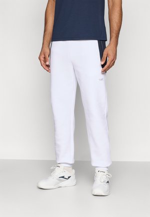 Biele športové nohavice so slim fit strihom, s bočnými sieťovinovými panelmi, v kombinácii s bielymi teniskami a námorníckym tričkom. Viditeľný jemný logotyp.