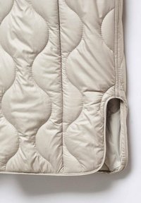 Beige quiltet stof med et bølget mønster, der har en sidelomme og en glat tekstur. Kanterne er syet for holdbarhed.