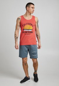 Rød tanktop med California-grafik og gult solmotiv, kombineret med blå shorts med logo. Båret med sorte atletiksko.