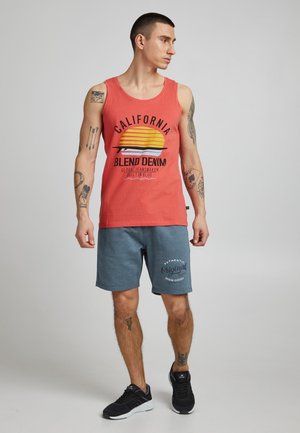 Red tank top with California graphic and yellow sun design, paired with blue shorts featuring a logo. Worn with black athletic shoes.