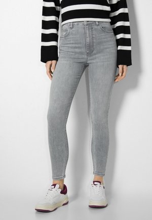 Light grey skinny jeans with a high waist and subtle fading. Paired with white sneakers featuring purple accents and a black striped sweater.