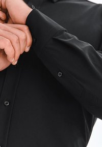 Czarna koszula z długim rękawem o gładkiej fakturze, mankietach na guziki oraz dopasowanym kroju, z subtelnym połyskiem tkaniny.