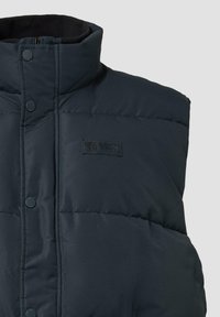 Navyblauw gewatteerd vest met hoge kraag, drukknoopsluiting, ritssluiting en een klein geborduurd logo op de borst.
