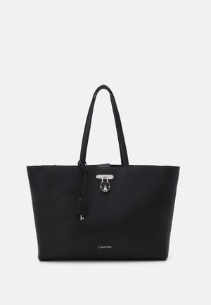 Sac cabas en cuir noir Calvin Klein avec double poignée, détail de cadenas et porte-clés argentés, texture grainée sur fond blanc.