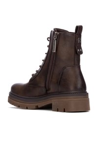 Botas de tobillo de cuero marrón con cordones, cremallera lateral y suela de goma gruesa. Presentan un lazo en la parte posterior y un sutil detalle de marca.
