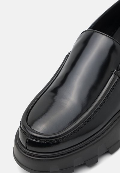 Chaussure en cuir verni noir avec un bout arrondi et une semelle en caoutchouc épaisse et texturée. Présente des détails cousus sur les côtés.